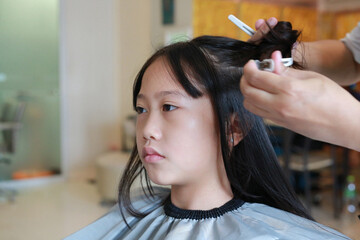 Asian preteen girl having her hair cut. Child sitting in beauty hair salon style for children....