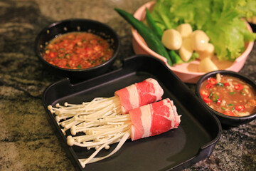 Raw roll with enoki mushroom and bacon for shabu or japanese hot pot in tray on table background.