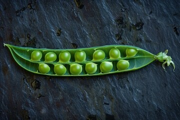 Open pea pod revealing fresh green peas resting on a dark stone background, showcasing the vibrant color and texture of the vegetable