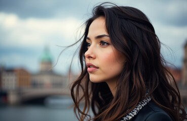 Fototapeta premium Woman with dark hair and serious expression looking to the side outdoors against cityscape background