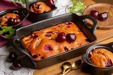 Rectangle form Cherry and Peach Clafoutis, homemade sweet pie with fresh fruits on a wooden table with white runner.