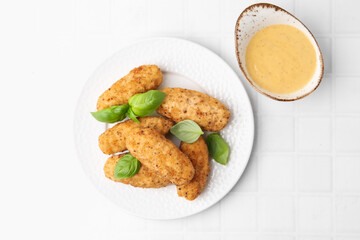 Tasty fried croquettes, basil and sauce on white tiled table, top view