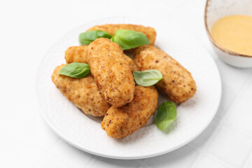 Tasty fried croquettes, basil and sauce on white tiled table, closeup