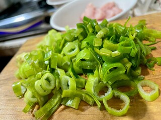 Close-up photo of sliced ​​leeks or spring onions on a wooden cutting board with a blurred...