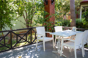 Outdoor patio with white furniture surrounded by lush greenery and natural sunlight for relaxation