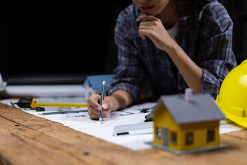 Female architect working in design office drawing house construction plans on wooden table in dark office.