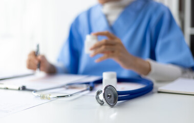 Female doctor reading and writing prescriptions in hospital office. The doctor is calculating the...