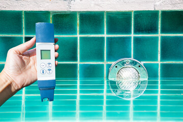 Quality digital water tester in girl hand over swimming pool light install on the wall, pool light illumination, quality water tester
