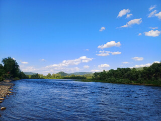 Peaceful river flows through lush green landscape under a clear blue sky in a serene natural setting