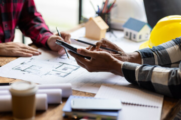 Architect using calculator calculating construction costs on blueprint. Architects collaborating at...
