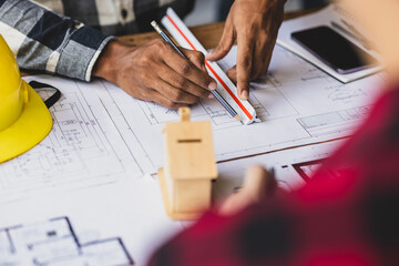 Architect using ruler and pencil reviewing blueprint of architectural project. Two architects are analyzing blueprints for a new building project, using a ruler and pencil to make measurement.