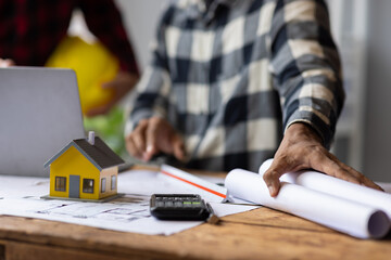 Architect using calculator calculating construction costs on blueprint. Architects collaborating at...