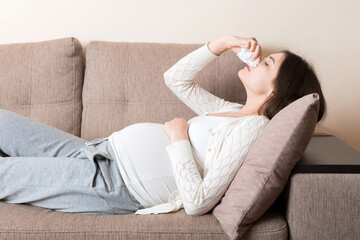 Sick pregnant woman blowing nose into tissue at home Healthy millennial healthcare concept