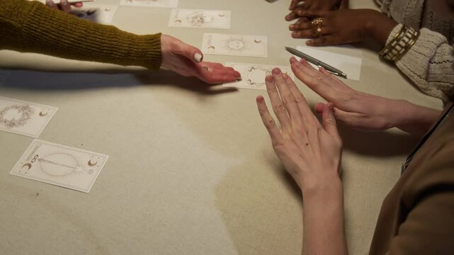 Over shoulder view of two biracial women looking at cards while tarot reader putting them on table