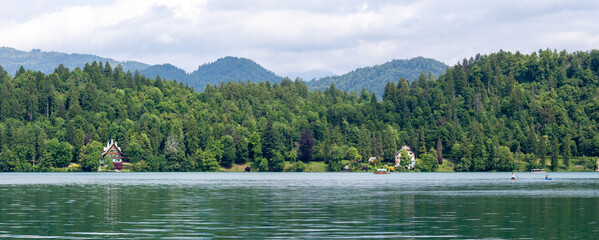 A wide panoramic view across the tranquil, green-hued waters of Lake Bled, revealing the lush,...