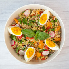 Freshly made spelt salad features roasted zucchini, carrots, onions, red peppers, and basil, topped with hard-boiled egg and dressed with lemon juice and olive oil.