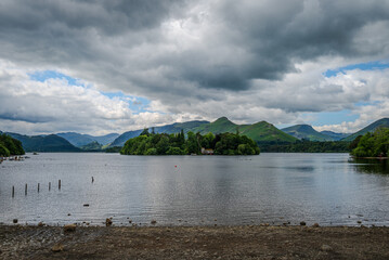 A summer landscape unfolds from the shores of Derwentwater, with clouds drifting above and the...