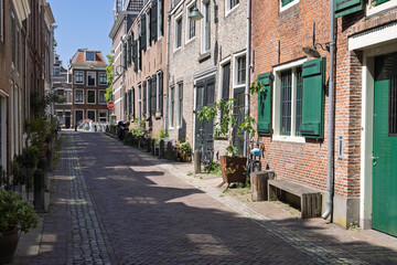 Fototapeta premium Quiet, sunny street in a historic Dutch city Gouda, lined with traditional brick houses featuring green shutters and charming details.