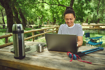 Woman Working Outdoors on a Laptop in a Scenic Forest Setting