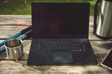 Laptop on Wooden Table Outdoors with Hiking Gear and Coffee