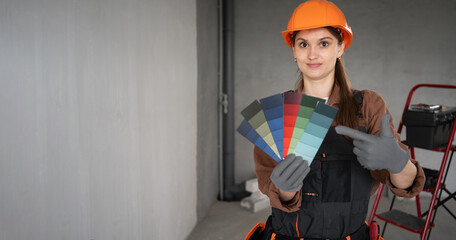 female painter in workwear holding color palette samples pointing finger and looking at camera with smile making house renovation