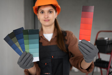Female painter in workwear holding color palette samples smiling at camera while working indoors