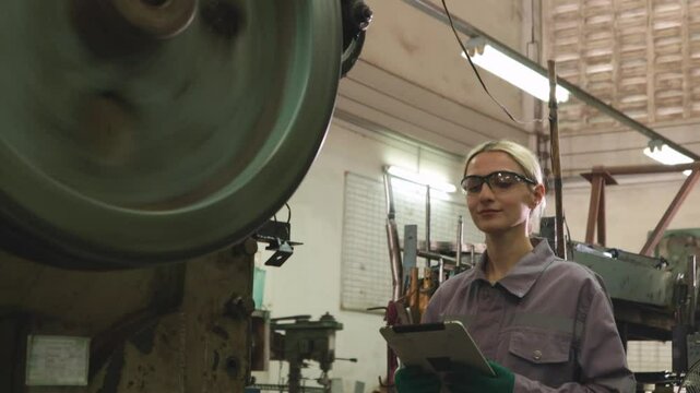 Female lathe operator wearing safety glasses to protect from metal chips while carefully operating metal stamping machine working on thin sheet metal in parts manufacturing plant.