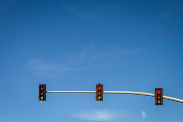 Three traffic lights hang on a horizontal pole against a vibrant blue sky on a clear day in the...
