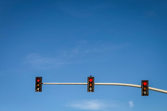 Three traffic lights hang on a horizontal pole against a vibrant blue sky on a clear day in the United States. Minimalist composition with strong contrast and copy space.