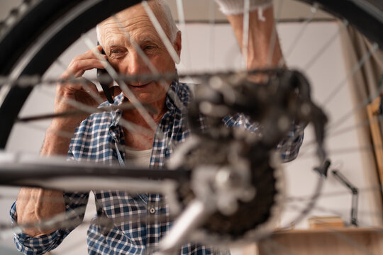 Retired man repairing bike talk on phone with mechanic, at home interior. smartphone call to hotline while fixing bicycle - Powered by Adobe