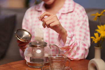 Asian Woman Enjoying Tea with Tea Bag in Glass Teapot for Relaxation and Healthy Lifestyle Drinking Herbal Beverage at Home Concept