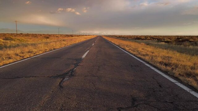 Asphalt road across the desert at sunrise. Drone view moving forward and climbing.