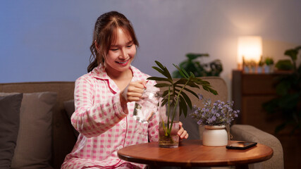 Asian Woman Watering Plants Indoor for Home Garden Care Wellness Hobby in Morning at Home as Part of Daily Longevity Lifestyle Habit with Water Glass