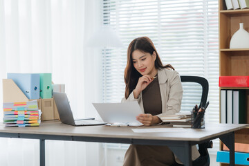 Focused Businesswoman Reviewing Documents: A young businesswoman sits at her desk, thoughtfully...
