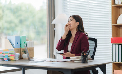 Tired Office Moment: A woman in a modern office desk yawns tiredly, showcasing the candid moments...