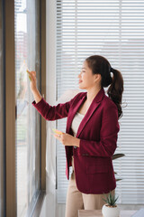 Smart Professional Woman at the Window: A confident professional woman stands by a large window,...