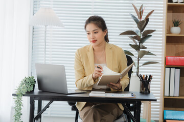 Working from Home: An Asian woman, immersed in her work. she is diligently engrossed in both a...