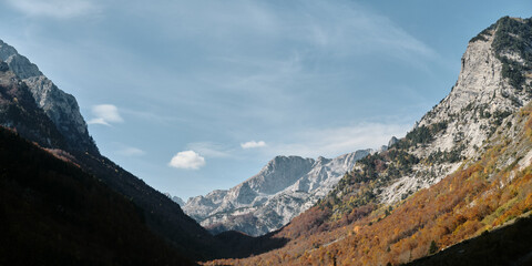Sharp ridges and colorful forested slopes of the Prokletije mountains in autumn, captured in warm...