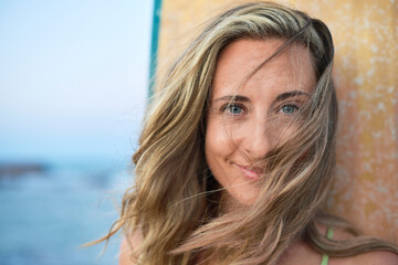 Blonde woman with piercing blue eyes gazes directly at the camera, showing a confident and...