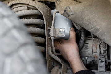 Mechanic's hand reaches out to install or remove an oil filter on the underbody of a car. Changing an oil filter