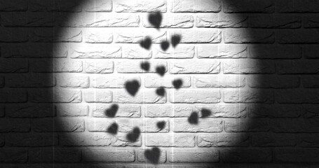 Hearts cast shadows on a white textured wall, illuminated by a  spotlight