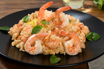 Shrimp risotto with lemon and basil on a black plate on a wooden table