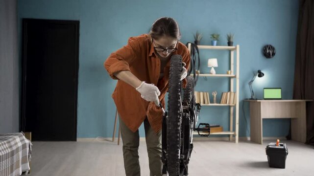 Woman repairing bicycle at home fixing wheel with wrench in room interior. Bicycle repair and maintenance