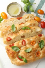 Cut delicious focaccia with tomatoes, basil and oil on table, flat lay