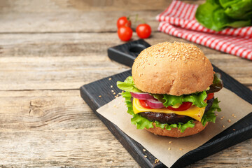 Delicious hamburger with patty and cheese on wooden table, closeup. Space for text
