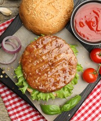 Delicious hamburger patty, bun, vegetables and spices on table, flat lay