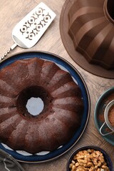 Tasty chocolate bundt cake, walnuts, cocoa powder and server on wooden table, flat lay
