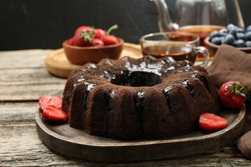 Tasty chocolate bundt cake with glaze, tea and berries on wooden table