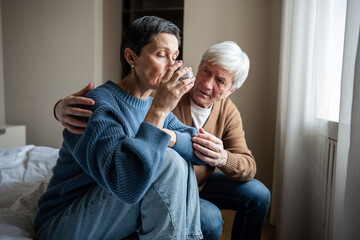 Upset grieving woman drinking water with trembling hand while elderly man comforts her with...