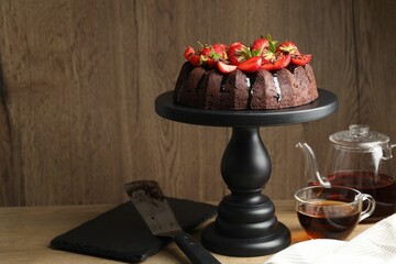 Delicious chocolate bundt cake with strawberries and tea on wooden table